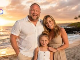 Alex Jones posing with his wife Erika Wulff Jones and their young daughter on a beach during a beautiful sunset.