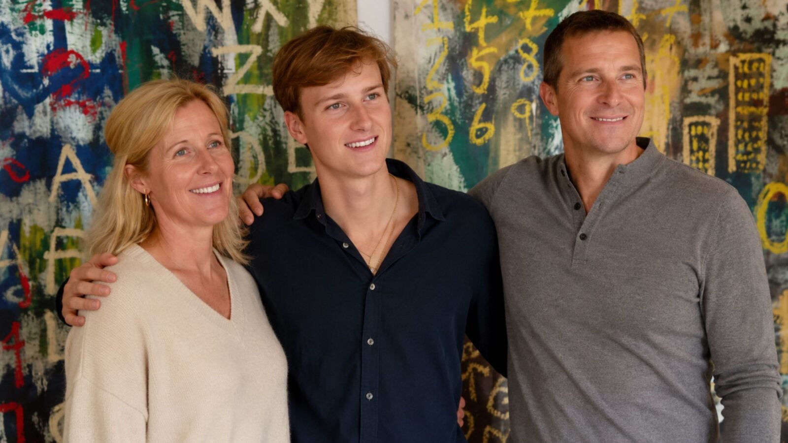Jesse Grylls smiling and standing confidently between his parents, Shara and Bear Grylls, in front of a colorful abstract expressionist painting.