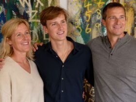 Jesse Grylls smiling and standing confidently between his parents, Shara and Bear Grylls, in front of a colorful abstract expressionist painting.