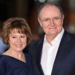 British actor Jim Broadbent smiling alongside his wife, artist Anastasia Lewis, at a public red carpet event.