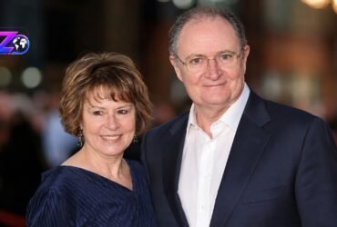 British actor Jim Broadbent smiling alongside his wife, artist Anastasia Lewis, at a public red carpet event.