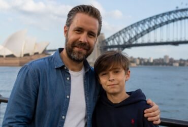 Actor Paddy Considine standing next to his son, musician Joseph Considine, smiling together with the Sydney Harbour Bridge in the background.