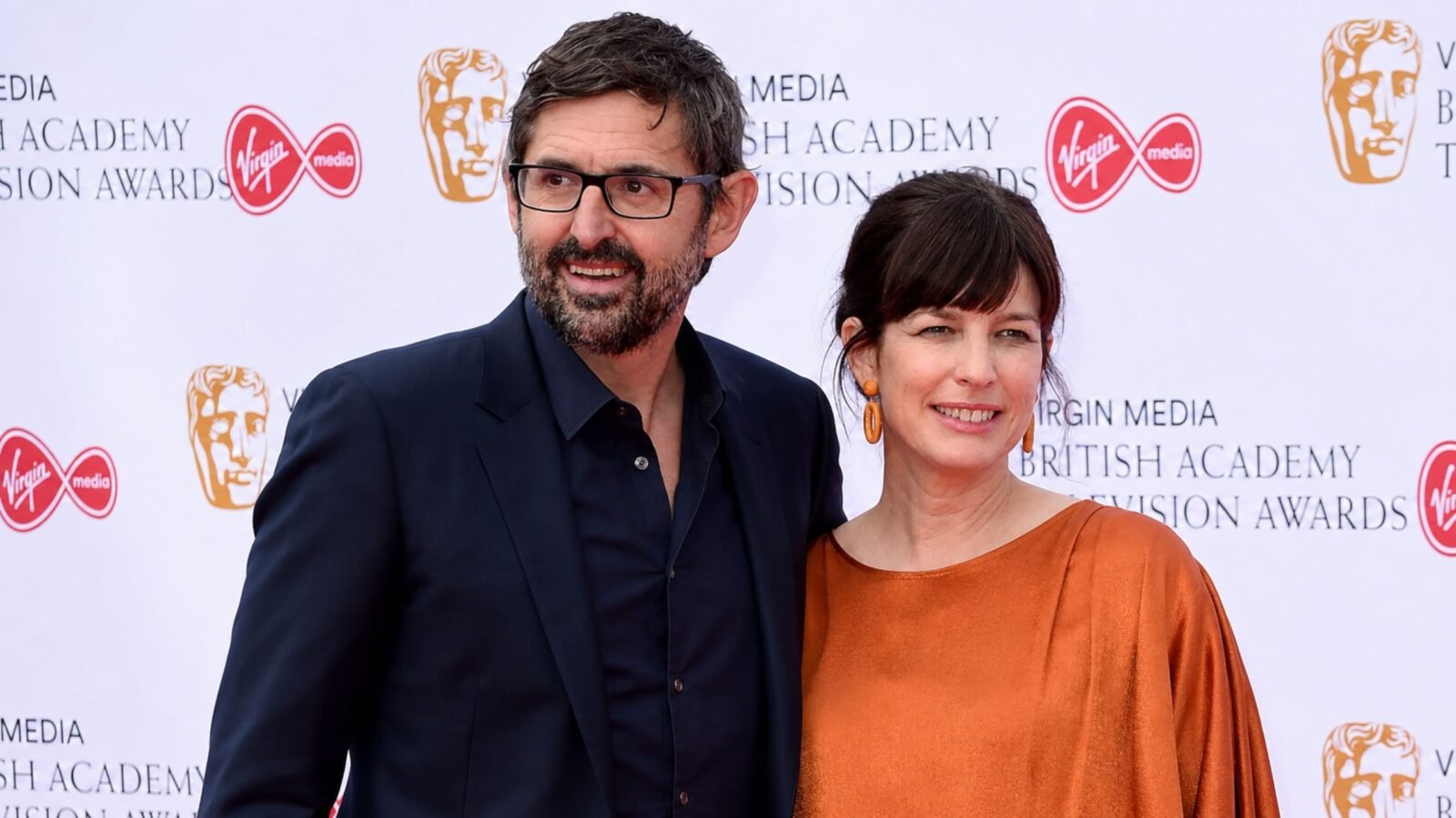 Documentary filmmaker Louis Theroux and his wife, executive producer Nancy Strang, smiling together on the red carpet at the Virgin Media British Academy Television Awards.