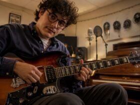 British-Italian alt-folk musician Luca Firth playing an electric guitar in a rustic recording studio.
