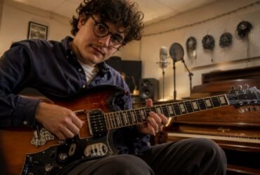 British-Italian alt-folk musician Luca Firth playing an electric guitar in a rustic recording studio.