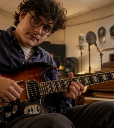 British-Italian alt-folk musician Luca Firth playing an electric guitar in a rustic recording studio.