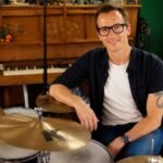 Professional drummer Luke Bullen smiling in his residential recording studio sitting next to his drum kit