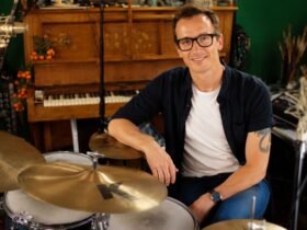 Professional drummer Luke Bullen smiling in his residential recording studio sitting next to his drum kit