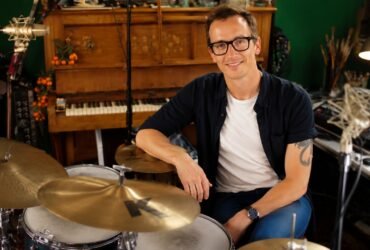 Professional drummer Luke Bullen smiling in his residential recording studio sitting next to his drum kit