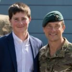 Marmaduke Grylls posing next to his father, Bear Grylls, who is dressed in military camouflage.