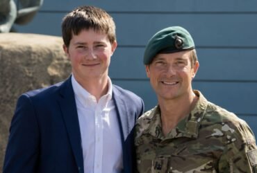 Marmaduke Grylls posing next to his father, Bear Grylls, who is dressed in military camouflage.