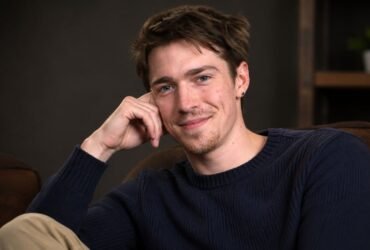 Portrait of emerging British actor Patrick Alwyn smiling gently while resting his head on his hand.