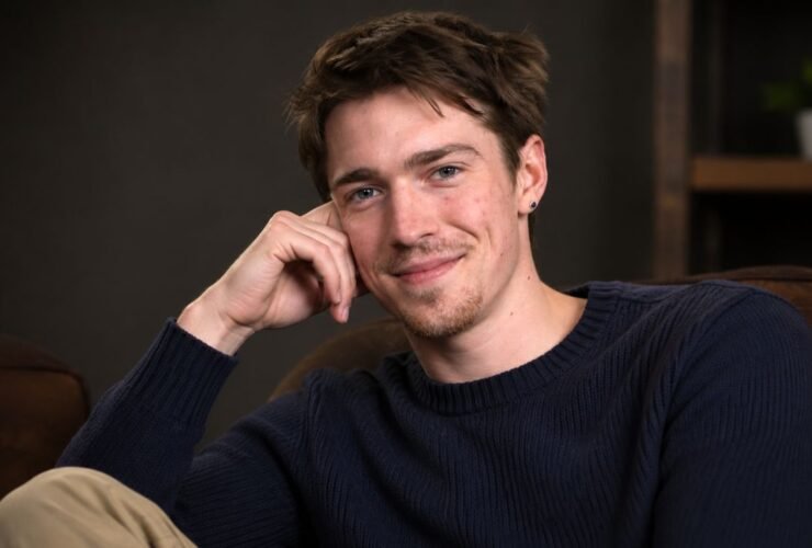 Portrait of emerging British actor Patrick Alwyn smiling gently while resting his head on his hand.