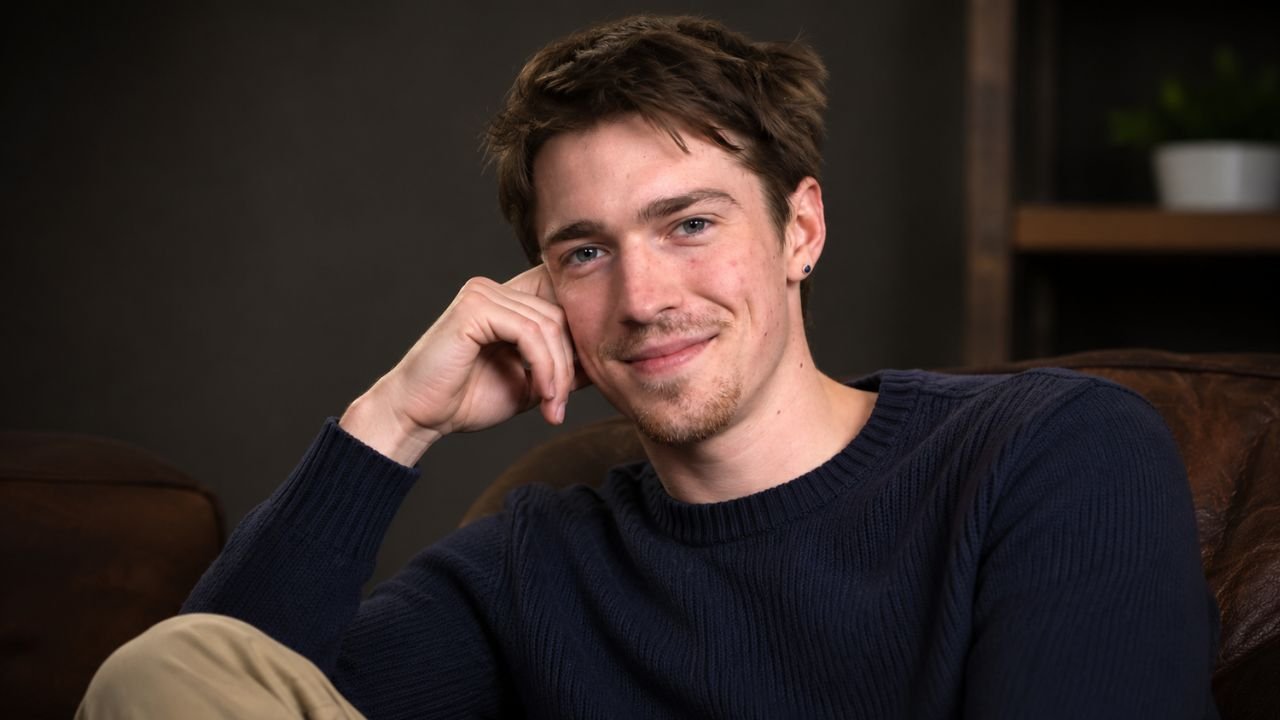 Portrait of emerging British actor Patrick Alwyn smiling gently while resting his head on his hand.