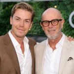 British actor Will Poulter standing alongside his father, Professor Neil Poulter, who is wearing glasses and a light-colored suit jacket at a public event.