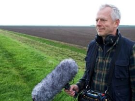 Documentary filmmaker Richard Alwyn holding a professional boom microphone and wearing headphones while filming in an open field.