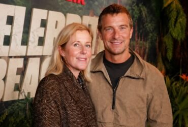 Shara Grylls smiling next to her husband, British adventurer Bear Grylls, at a public red carpet event.