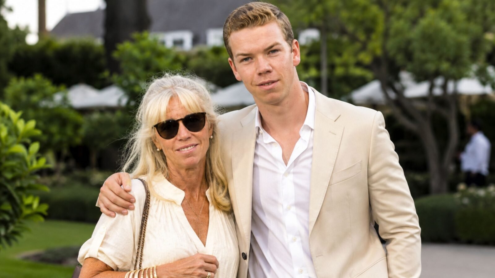 Actor Will Poulter standing outdoors next to his mother, Caroline Poulter, who is wearing sunglasses and a light-colored blouse.